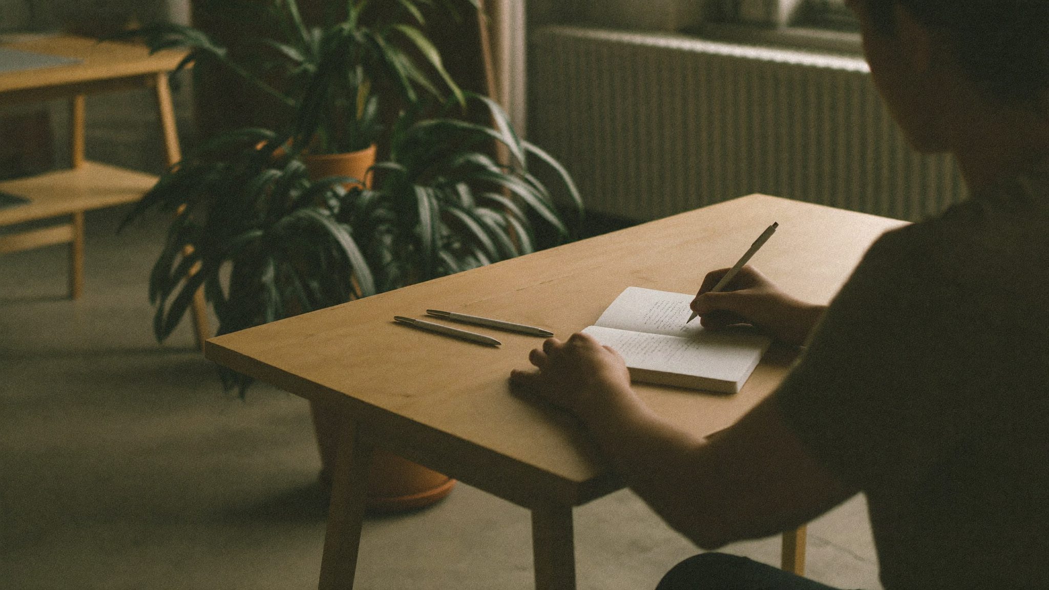 Secretária de estúdio com mãos a tomar notas, caderno e plantas